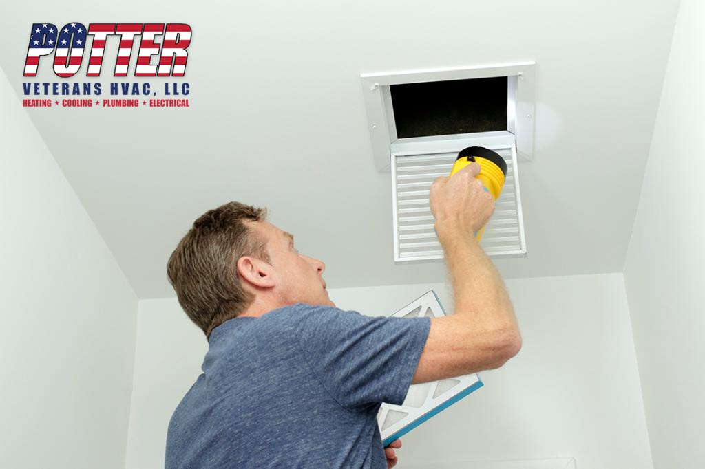 Man inspecting air ducts shining a flashlight through a small square ceiling vent into ducting pipes.