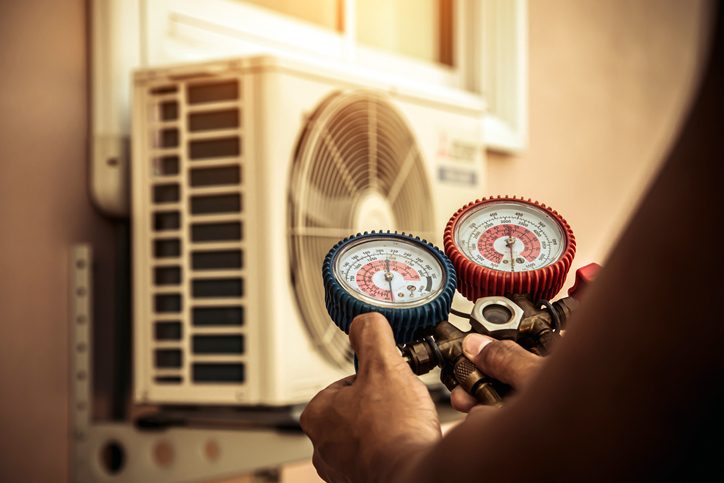 Air repair mechanic using measuring manifold gauge equipment for filling home air conditioner after cleaner and checking maintenance outdoor air compressor unit.