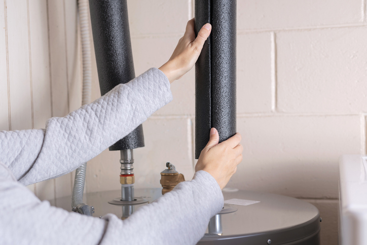 Person installing pipe insulation on a water heater